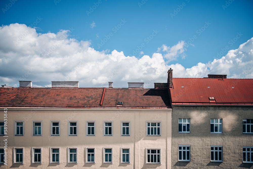 Fototapeta premium Old european town houses with many similar windows on facade and terracotta tile roofs against blue sky with white clouds in sunny day.