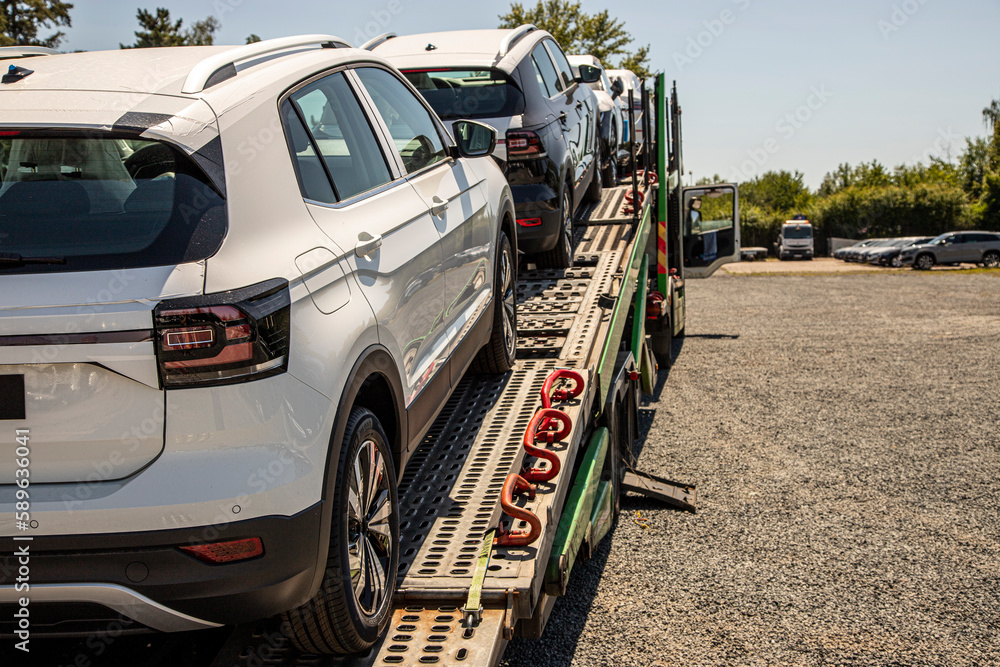 New white crossover - SUV on car carrier trailer, car-carrying trailer, car hauler, auto transport trailer, semi-trailer. Rear view car. Rear view trailer. Visible taillamps. - obrazy, fototapety, plakaty 