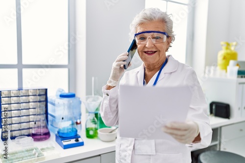 Senior grey-haired woman wearing scientist uniform talking on the smartphone at laboratory