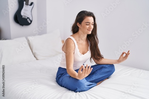 Young hispanic woman doing yoga exercise sitting on bed at bedroom