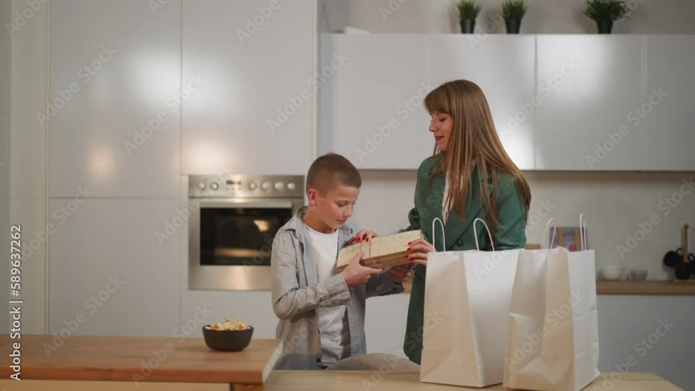 Smiling pleasant woman in business suit takes out food from bags. Schoolboy helps mom taking waffles, cookies and cupcakes. Preparing for family dinner Smiling pleasant woman in business suit takes out food from bags. Schoolboy helps mom taking waffles, cookies and cupcakes. Preparing for family dinner