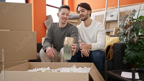 Canvas Print Two men couple unpacking cardboard box at new home