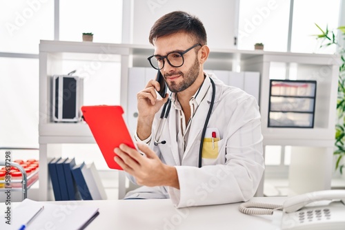 Wallpaper Mural Young hispanic man doctor using touchpad talking on samrtphone at clinic Torontodigital.ca