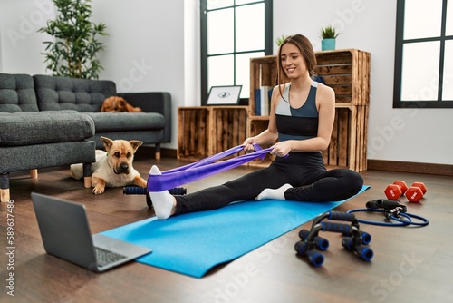 Young hispanic woman smiling confident having online traininig using elastic band at home photo