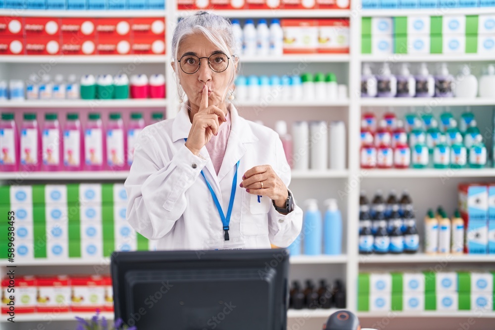 Middle age woman with tattoos working at pharmacy drugstore asking to be quiet with finger on lips. silence and secret concept. Middle age woman with tattoos working at pharmacy drugstore asking to be quiet with finger on lips. silence and secret concept.