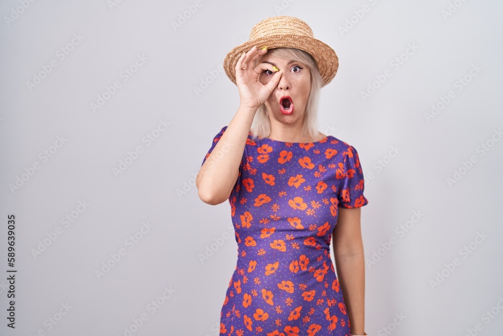 Young caucasian woman wearing flowers dress and summer hat doing ok gesture shocked with surprised face, eye looking through fingers. unbelieving expression. Young caucasian woman wearing flowers dress and summer hat doing ok gesture shocked with surprised face, eye looking through fingers. unbelieving expression.