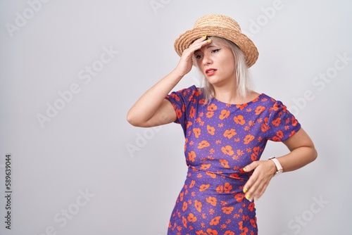Young caucasian woman wearing flowers dress and summer hat touching forehead for illness and fever, flu and cold, virus sick