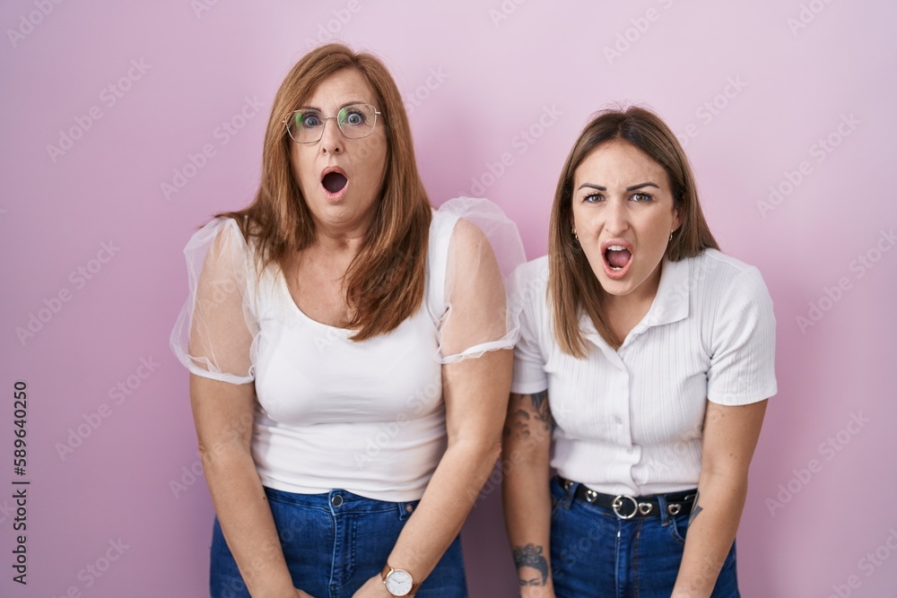 Hispanic mother and daughter wearing casual white t shirt over pink background afraid and shocked with surprise and amazed expression, fear and excited face. Hispanic mother and daughter wearing casual white t shirt over pink background afraid and shocked with surprise and amazed expression, fear and excited face.