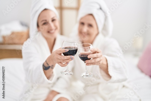 Mother and daughter wearing bathrobe drinking glass of wine at bedroom