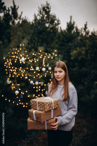 beautiful girl in winter pine forest. decorates the Christmas tree with bright lights and toys in the forest. Christmas presents in the forest under the tree. Christmas tree lights. New Year's decor 