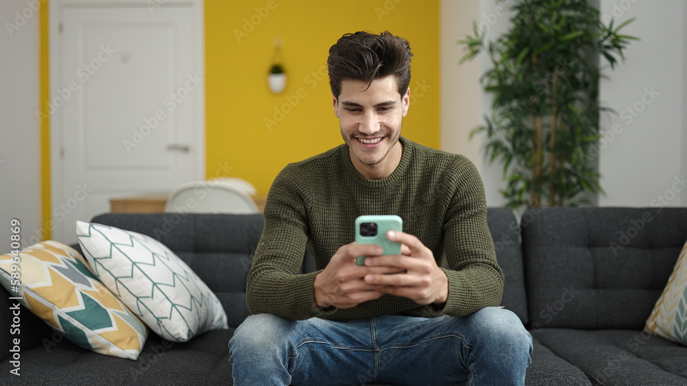 Young hispanic man using smartphone sitting on sofa at home Young hispanic man using smartphone sitting on sofa at home