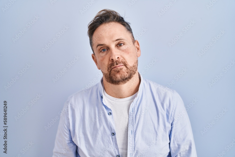 Middle age caucasian man standing over blue background looking sleepy and tired, exhausted for fatigue and hangover, lazy eyes in the morning. Middle age caucasian man standing over blue background looking sleepy and tired, exhausted for fatigue and hangover, lazy eyes in the morning.