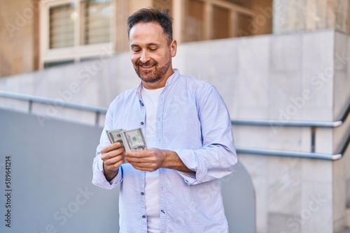 Young caucasian man smiling confident counting dollars at street