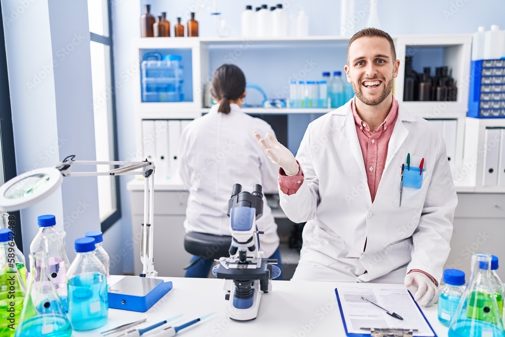 Young man working at scientist laboratory celebrating achievement with happy smile and winner expression with raised hand Young man working at scientist laboratory celebrating achievement with happy smile and winner expression with raised hand