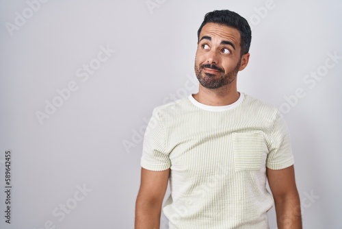 Hispanic man with beard standing over isolated background smiling looking to the side and staring away thinking.