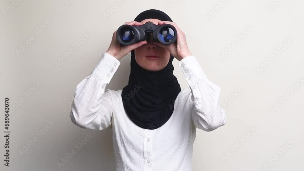Young woman in hijab looking through binoculars on white background. Young woman in hijab looking through binoculars on white background.