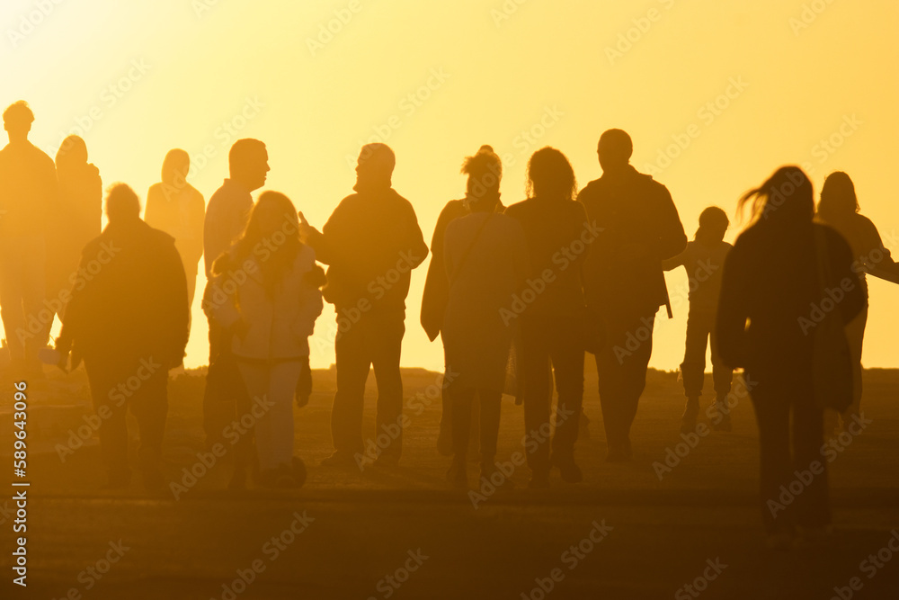 Silhouettes of people in yellow light of a bright orange sunset