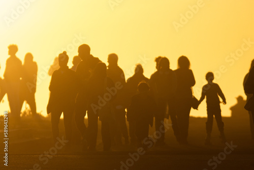 The silhouette of a crowd of people goes towards the yellow bright sunset