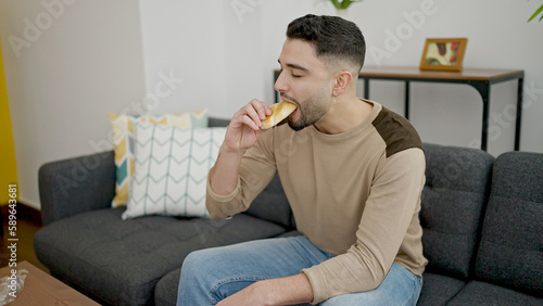 Young arab man eating cake sitting on sofa at home