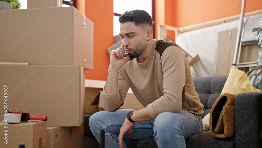 Young arab man sitting on sofa with doubt expression at new home Young arab man sitting on sofa with doubt expression at new home