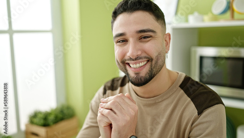 Young arab man smiling confident sitting on table at home