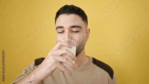 Young arab man drinking milk over isolated yellow background