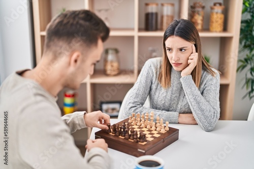Man and woman couple playing chess sitting on table at home