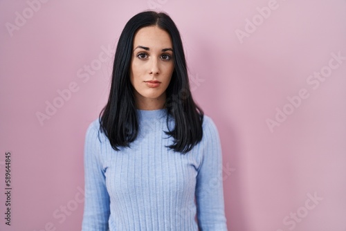 Hispanic woman standing over pink background relaxed with serious expression on face. simple and natural looking at the camera.
