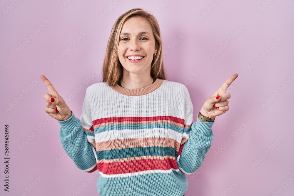 Young blonde woman standing over pink background smiling confident pointing with fingers to different directions. copy space for advertisement Young blonde woman standing over pink background smiling confident pointing with fingers to different directions. copy space for advertisement