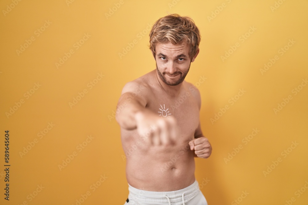 Caucasian man standing shirtless wearing sun screen punching fist to fight, aggressive and angry attack, threat and violence