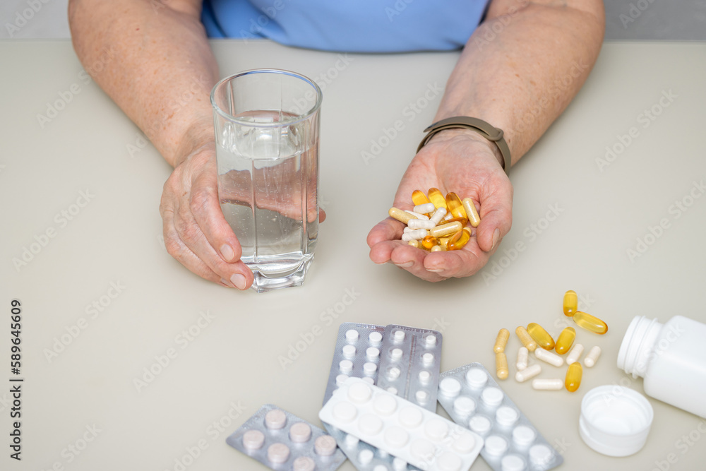 Senior woman with wrinkled old hands at the table holding various capsules and vitamins, full palm with pills for treatment. Healthcare and medicine concept Senior woman with wrinkled old hands at the table holding various capsules and vitamins, full palm with pills for treatment. Healthcare and medicine concept