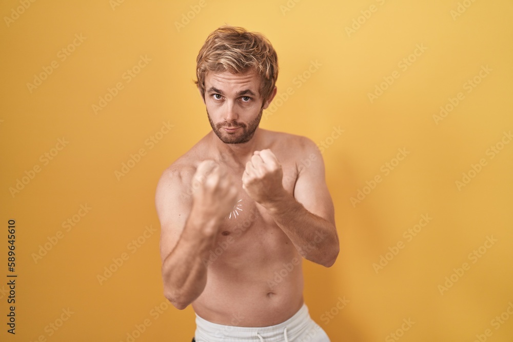Caucasian man standing shirtless wearing sun screen ready to fight with fist defense gesture, angry and upset face, afraid of problem