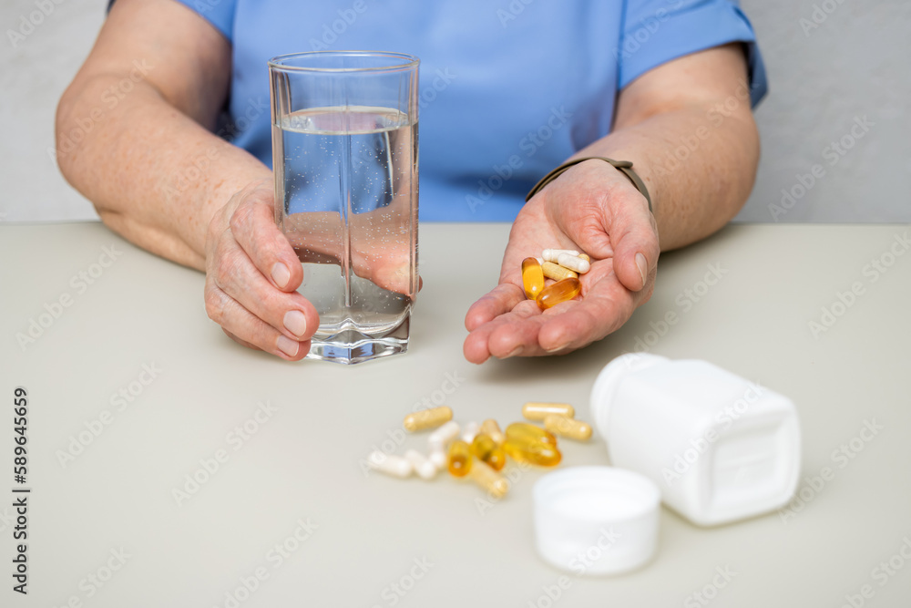 Senior woman with wrinkled old hands at the table holding various capsules, vitamins and pills for treatment. Healthcare and medicine concept Senior woman with wrinkled old hands at the table holding various capsules, vitamins and pills for treatment. Healthcare and medicine concept