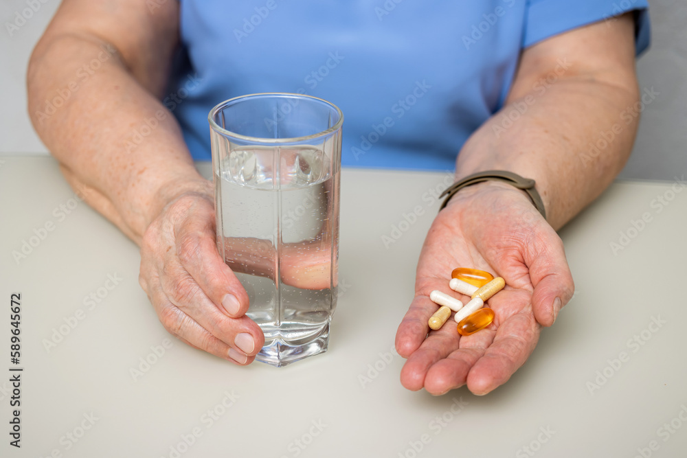 Senior woman with wrinkled old hands at the table holding various capsules, vitamins and pills for treatment. Healthcare and medicine concept Senior woman with wrinkled old hands at the table holding various capsules, vitamins and pills for treatment. Healthcare and medicine concept