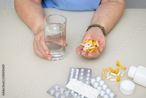 Senior woman with wrinkled old hands at the table holding various capsules and vitamins, full palm with pills for treatment. Healthcare and medicine concept