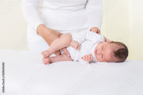 Loving Mother or Physiotherapist Doing Lateral Exercises To Newborn Baby Girl On Bed At Home