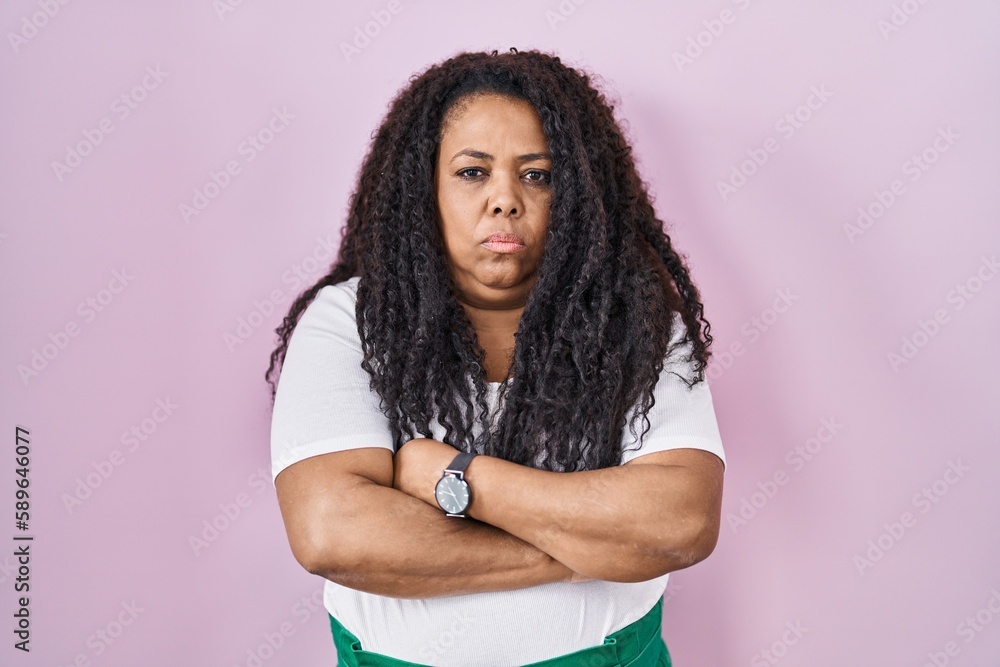 Plus size hispanic woman standing over pink background skeptic and nervous, disapproving expression on face with crossed arms. negative person. Plus size hispanic woman standing over pink background skeptic and nervous, disapproving expression on face with crossed arms. negative person.