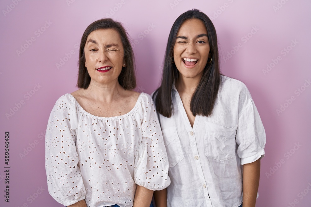 Hispanic mother and daughter together winking looking at the camera with sexy expression, cheerful and happy face. Hispanic mother and daughter together winking looking at the camera with sexy expression, cheerful and happy face.