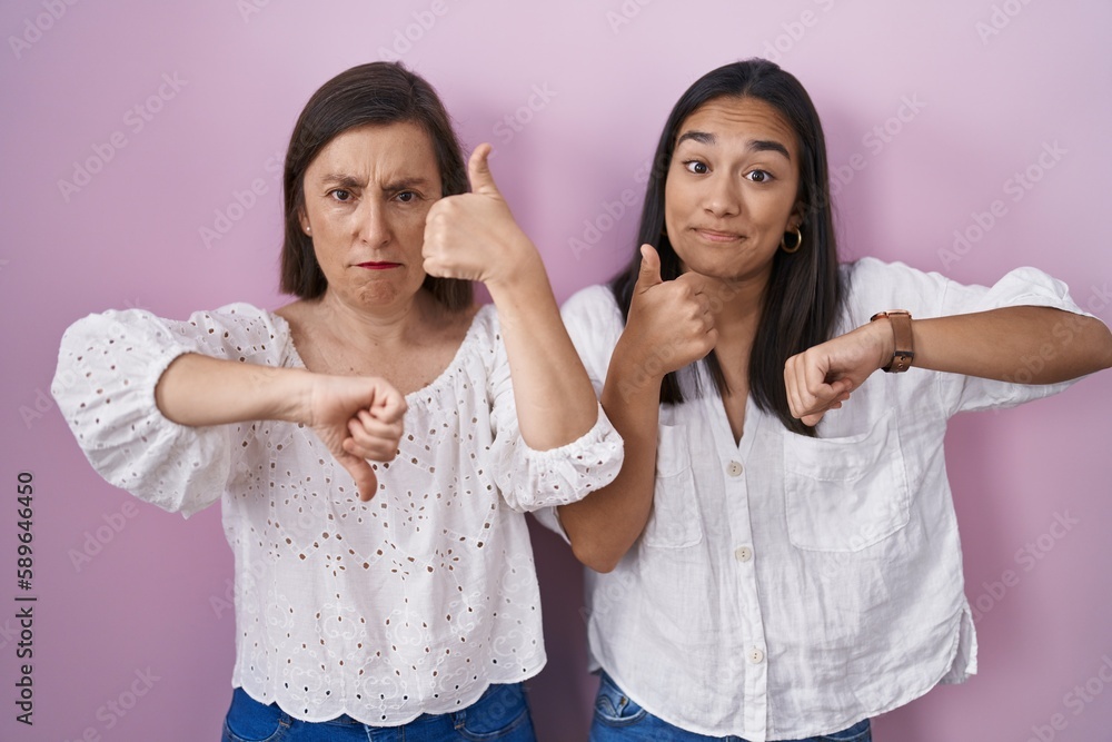 Hispanic mother and daughter together doing thumbs up and down, disagreement and agreement expression. crazy conflict Hispanic mother and daughter together doing thumbs up and down, disagreement and agreement expression. crazy conflict