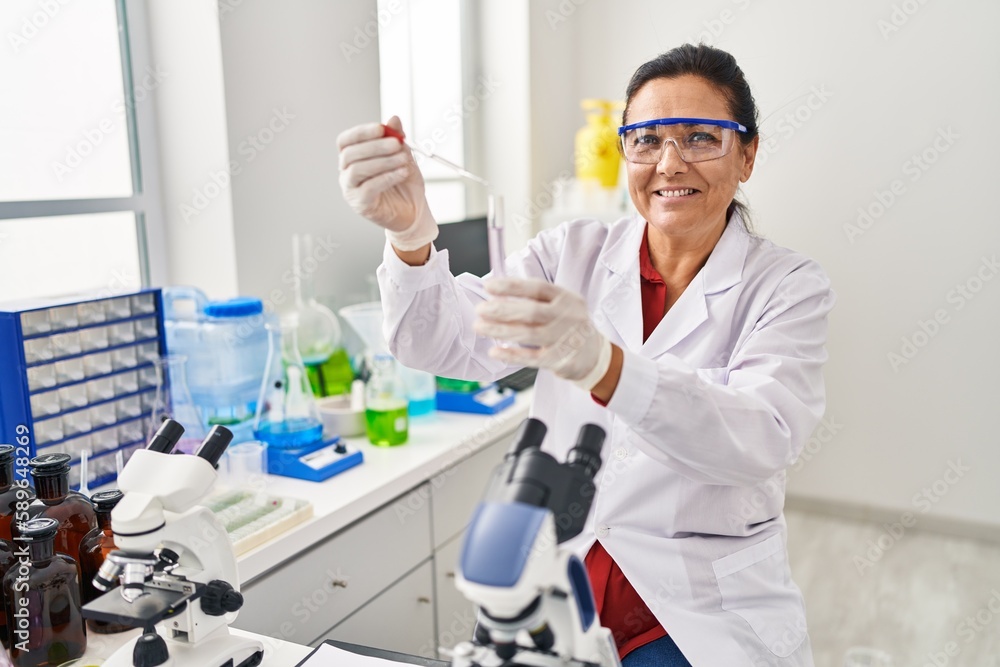 Middle age hispanic woman wearing scientist uniform using pipette at laboratory Middle age hispanic woman wearing scientist uniform using pipette at laboratory