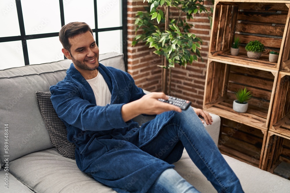 Young hispanic man watching tv sitting on sofa at home Young hispanic man watching tv sitting on sofa at home