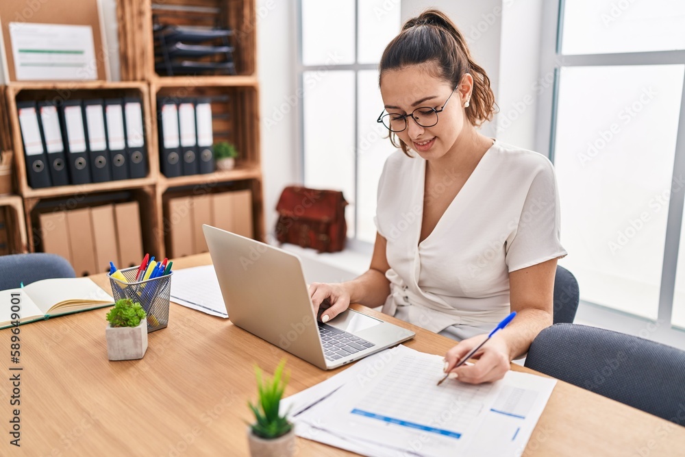 Young beautiful hispanic woman business worker using laptop writing on document at office Young beautiful hispanic woman business worker using laptop writing on document at office