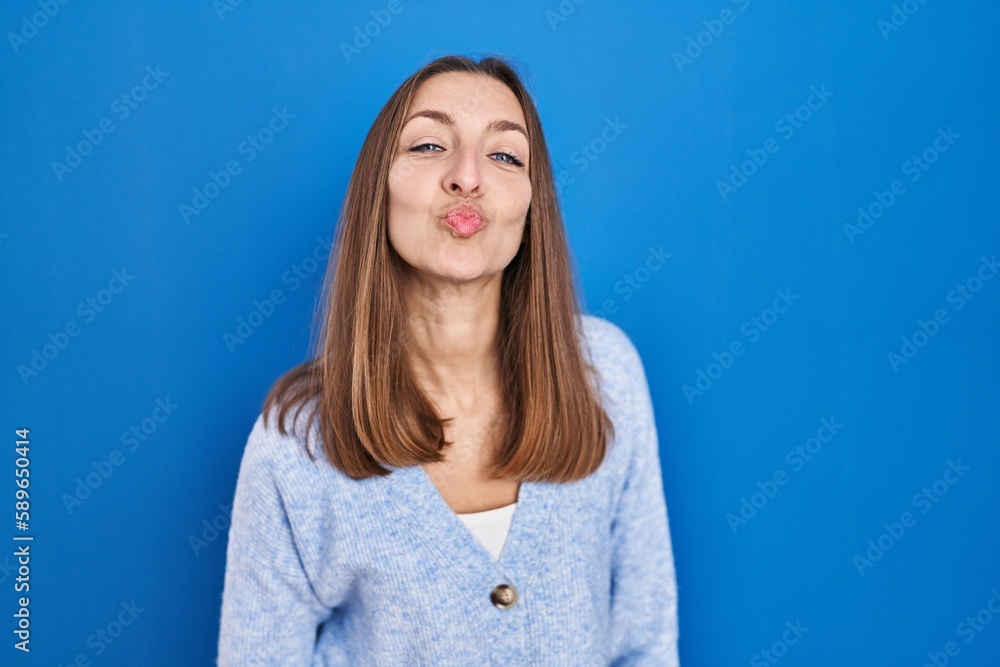 Young woman standing over blue background looking at the camera blowing a kiss on air being lovely and sexy. love expression. Young woman standing over blue background looking at the camera blowing a kiss on air being lovely and sexy. love expression.