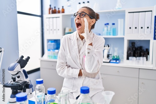 Young woman working at scientist laboratory clueless and confused with open arms  no idea and doubtful face.