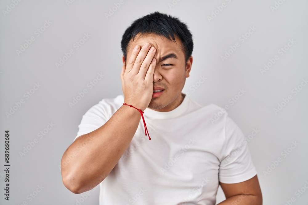Young chinese man standing over white background yawning tired covering half face, eye and mouth with hand. face hurts in pain. Young chinese man standing over white background yawning tired covering half face, eye and mouth with hand. face hurts in pain.