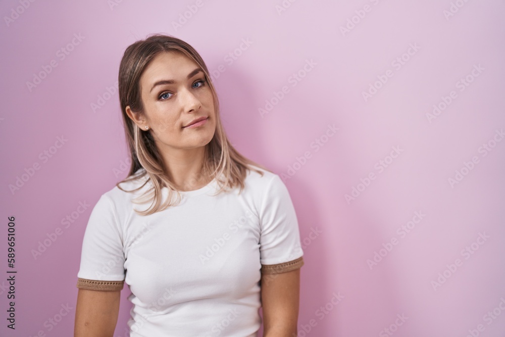 Blonde caucasian woman standing over pink background relaxed with serious expression on face. simple and natural looking at the camera. Blonde caucasian woman standing over pink background relaxed with serious expression on face. simple and natural looking at the camera.