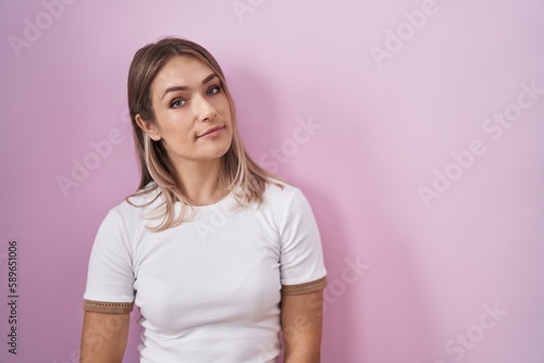 Blonde caucasian woman standing over pink background relaxed with serious expression on face. simple and natural looking at the camera.