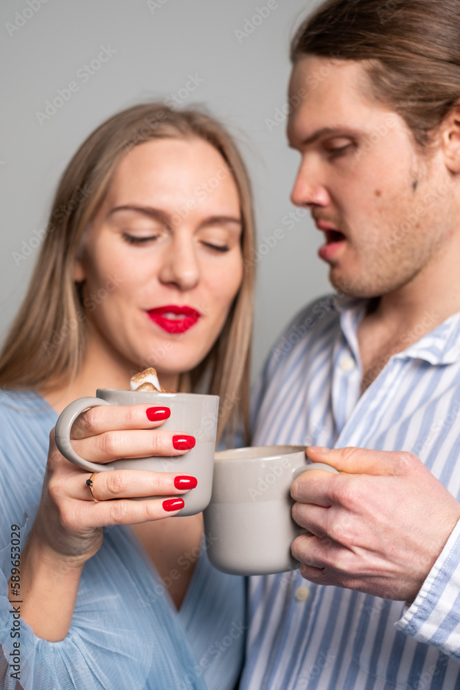 Surprised man and beautiful dreamy woman with red lips and nails and a ring on her finger. Young couple in light blue clothes drinking coffee. Copyspace Surprised man and beautiful dreamy woman with red lips and nails and a ring on her finger. Young couple in light blue clothes drinking coffee. Copyspace