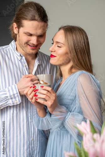 Beautiful young happy couple in light blue clothes enjoying coffee and each other s presence. Pink tulips in the corner in the foreground. Copyspace