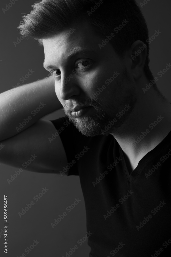 Close up black and white portrait of an attractive caucasian male model. He is wearing a black shirt and has blonde hair. He has a beard. 